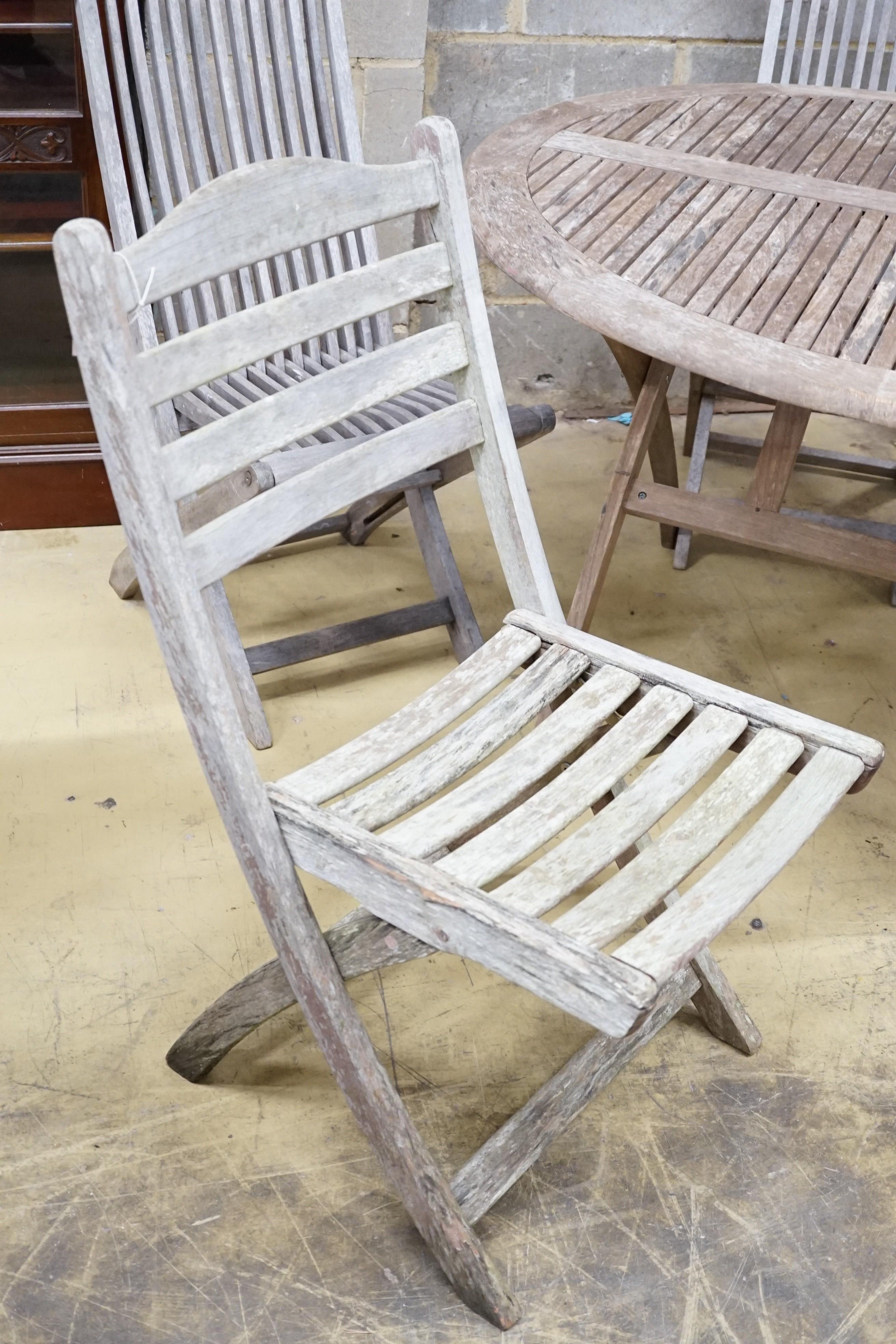 A weathered teak circular folding garden table, diameter 116cm and two pairs of folding chairs